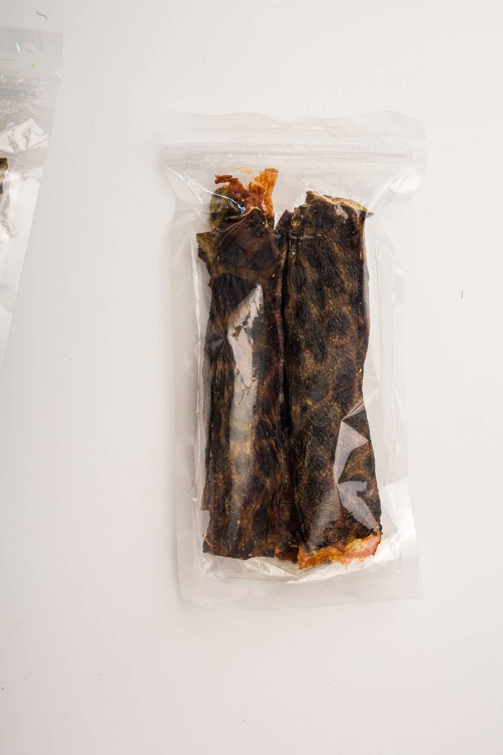 Two dried wolffish skin dog treats inside a clear plastic resealable bag, photographed on a plain white background.