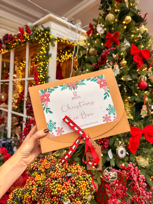 Christmas gift box with floral design and red ribbon held in front of a decorated Christmas tree.