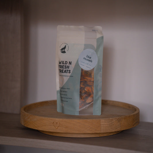 A stand-up pouch of Blue Mussels Wild N Fresh Treats for pets, displayed on a round wooden tray on a shelf.