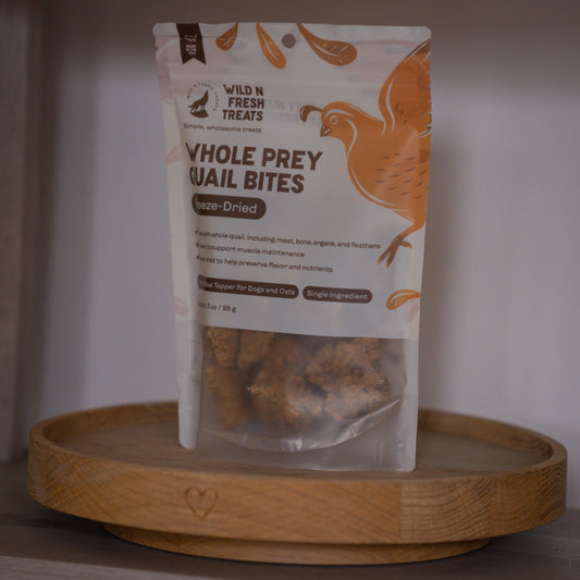 A stand-up pouch of Wild N Fresh Treats Whole Prey Quail Bites freeze-dried pet treats, displayed on a round wooden tray against a neutral indoor background.